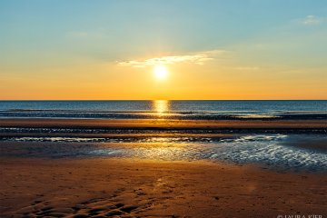Nordsee-Weite: Die Sonne neigt sich dem Horizont entgegen, wodurch der untere Teil des Himmels gelb gefärbt ist. Vereinzelte Wolken sind zu sehen. Unter der Sonne schimmert blau-gelb die Nordsee. Im Vordergrund der Strand von St. Peter-Ording